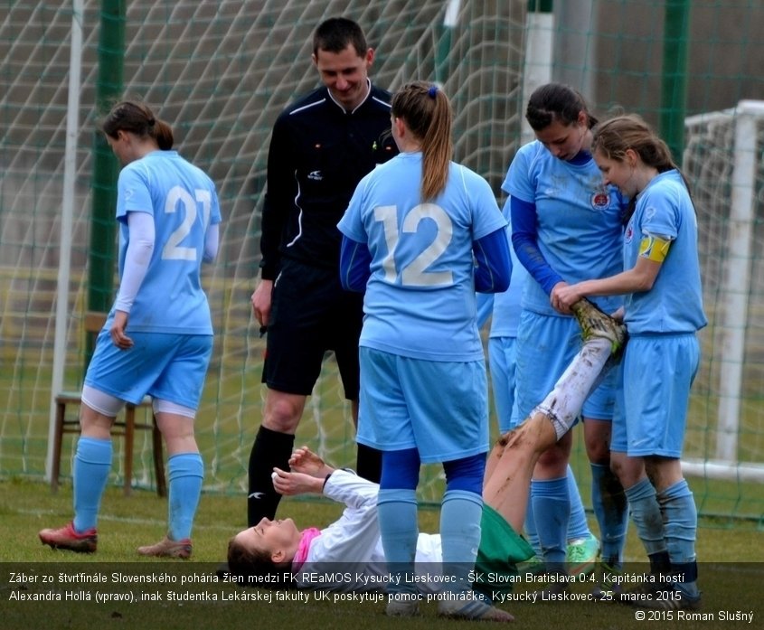 Záber zo štvrťfinále Slovenského pohária žien medzi FK REaMOS Kysucký Lieskovec - ŠK Slovan Bratislava 0:4. Kapitánka hostí Alexandra Hollá (vpravo), inak študentka Lekárskej fakulty UK poskytuje pomoc protihráčke. Kysucký Lieskovec, 25. marec 2015